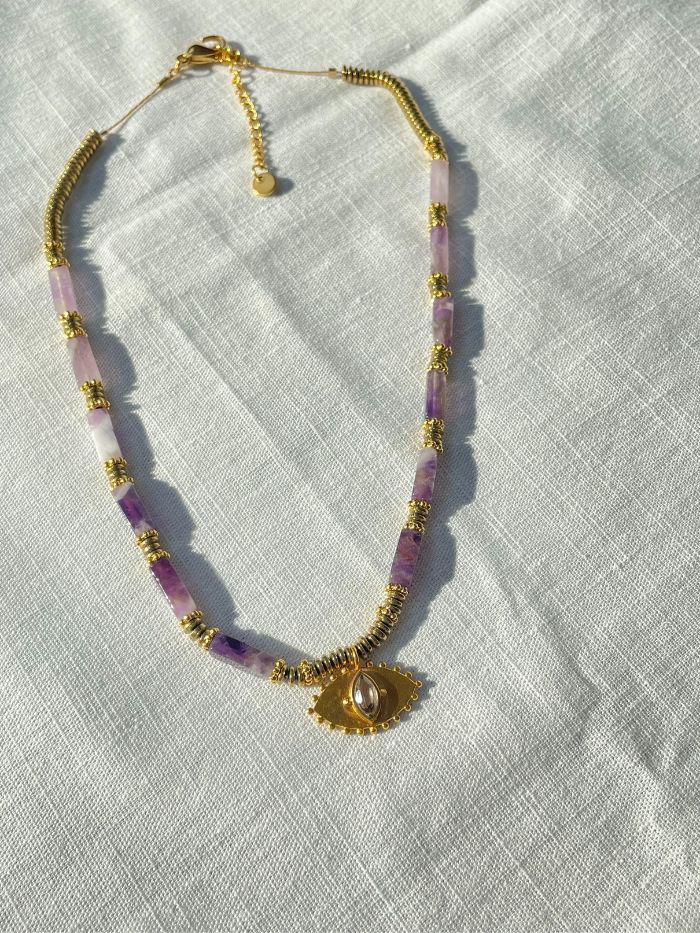 Craquez pour ce collier violet femme tendance AMELIA en perles fines d'Améthyste est composé de perles violette effet marbré de forme rectangle. Un collier à la fois chic et élégant tout en étant très moderne avec son pendentif en forme d'oeil et son Quartz fumé au centre. Ce collier fantaisie tendance est entièrement assemblé à la main par Axelle la créatrice des Jolis hasards. Collier fabriqué à Vincennes. Bijou fabriqué en France.